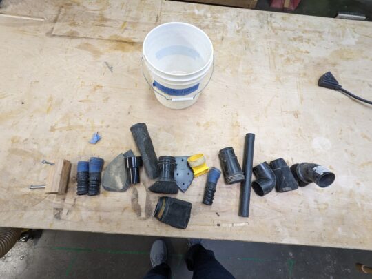 The various parts of the dust kit are spread out individually on the work bench in front of the dust kit bucket.