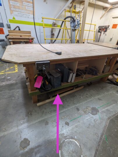 Arrow pointing to the location of the Ryobi router under the work bench.