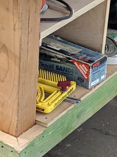 Under shelving with the box for the Ryobi detail sander. It is shown next to other tools.