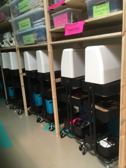 6 Janome Machines Lined Up Under Textile Shelving Storage