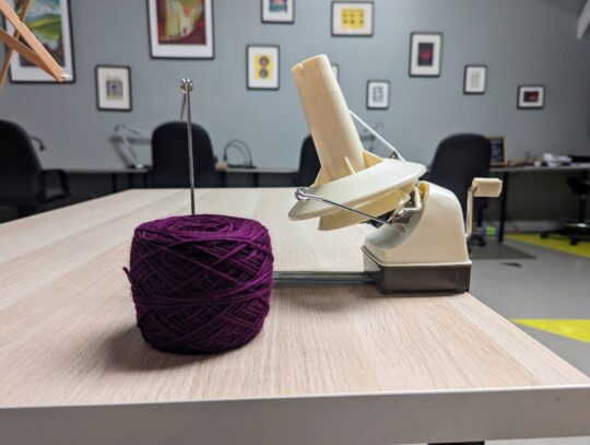 Photo of purple yarn cake next to the ball winder.